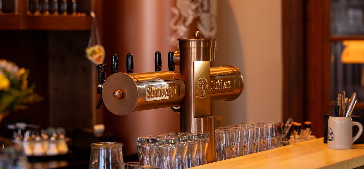 Bierzapfsäule mit mehreren Zapfhähnen und aufgereihten Biergläsern an der Bar im Starnberger Wirtshaus.