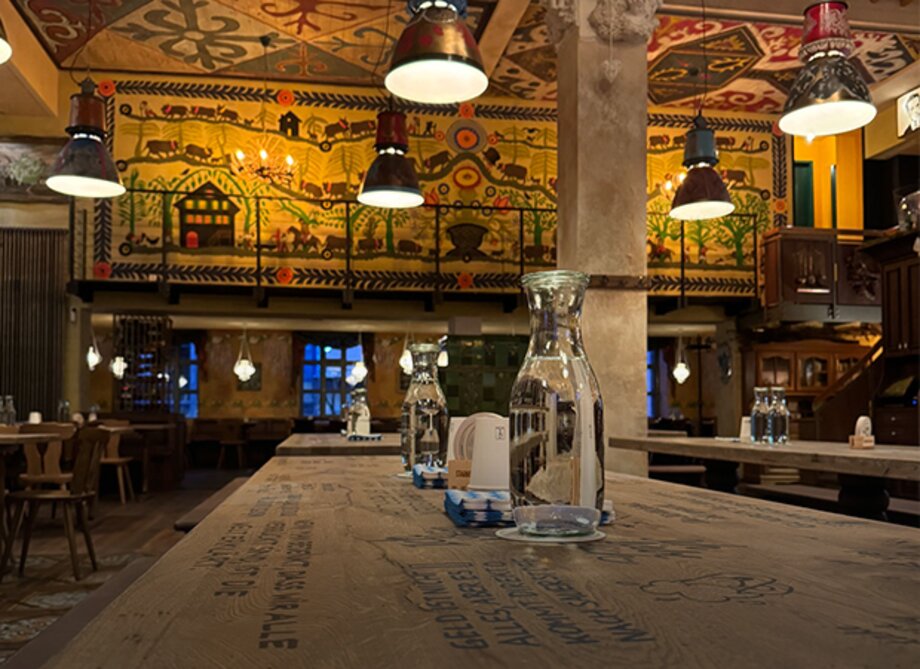 Innenraum eines traditionellen Starnberger Wirtshauses in Frankfurt mit langen Holztischen, Krügen und Wandmalereien mit ländlichen Motiven.