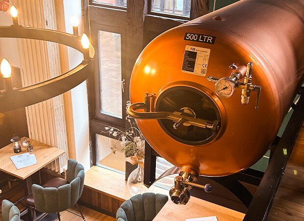 Kupferfarbener Braukessel mit Zapfhahn hängt oberhalb der Gaststube.