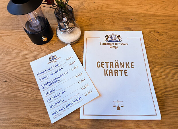 Getränkekarte auf weißem Papier liegt auf einem Holztisch.