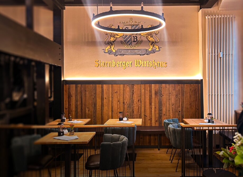 Innenraum des Starnberger Wirtshauses mit Holztischen, Stühlen und Kronleuchter an der Decke.